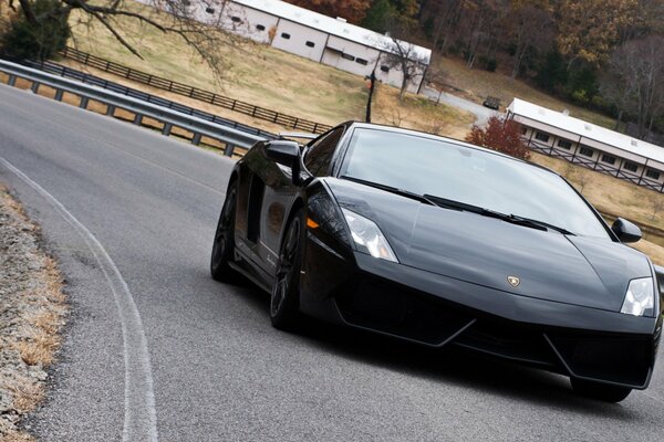 Un Lamborghini negro recorre la carretera con baches alrededor de los bordes en medio de un paisaje rústico otoñal