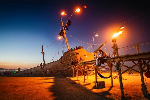 Al atardecer, un barco que se hunde con un mástil en llamas y personas en cubierta