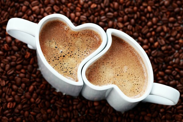 Dos tazas de café con forma de corazón en el fondo de los granos de café