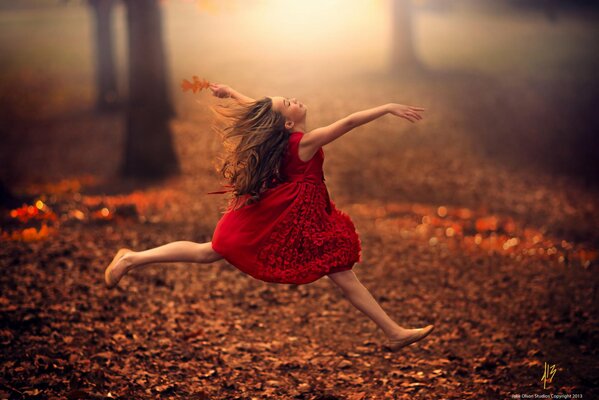 Una niña corre en un vestido rojo sobre las hojas