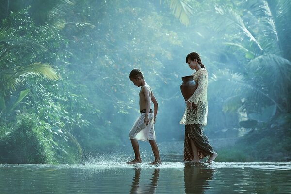 Niña con jarra y niño caminando por el río en la selva