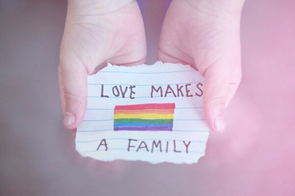 Dibujo de un arco iris en hojas de papel con una inscripción en las manos de un niño