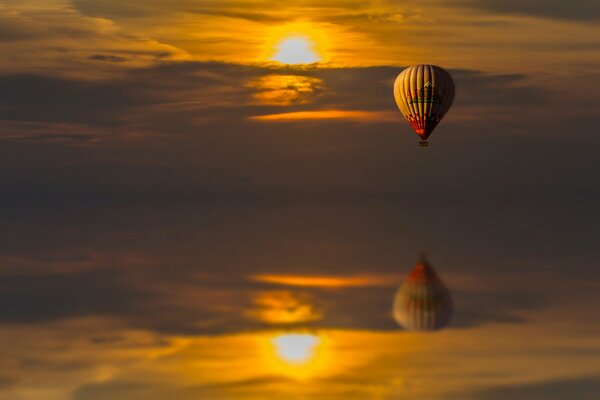 Reflejo en el agua de un globo que vuela al atardecer