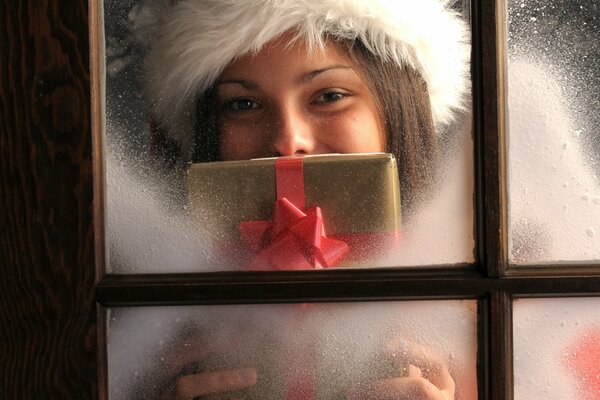 Una chica con una gorra y un regalo en la mano, mirando por la ventana